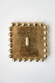 Decorative gold light switch cover with bead detailing on a white background