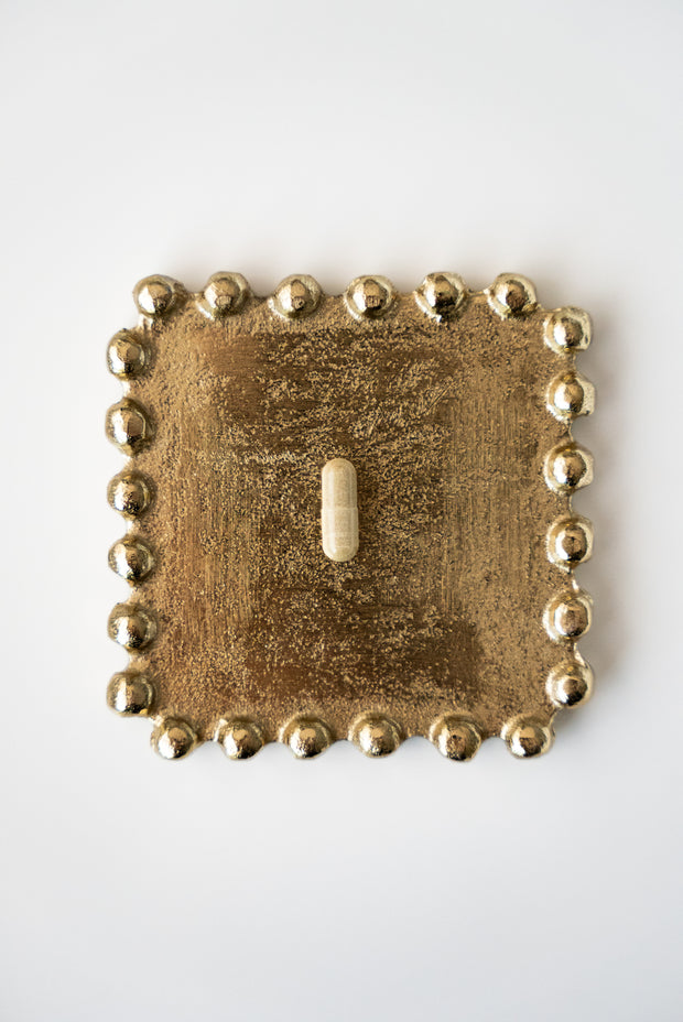 Decorative gold light switch cover with bead detailing on a white background
